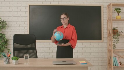 Woman teacher in classroom streaming live video lesson conference online using smartphone, holding globe in hand. Distant remote modern education.