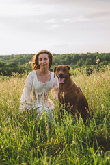 young cheerful woman playing with her dog outdoors in beautiful countryside field. Female and ridgeback dog walking and having fun