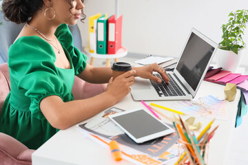 Young graphic designer with laptop and coffee working at table in office, closeup