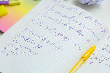 Open copybook with math formulas and pen on table, closeup