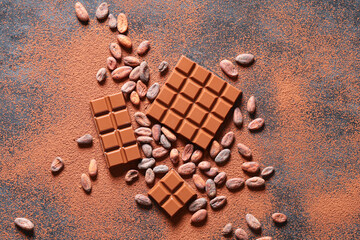 Sweet chocolate with cocoa beans and powder on dark background