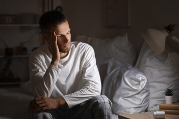 Fototapeta premium Young man suffering from insomnia and sitting on bed in bedroom at late night