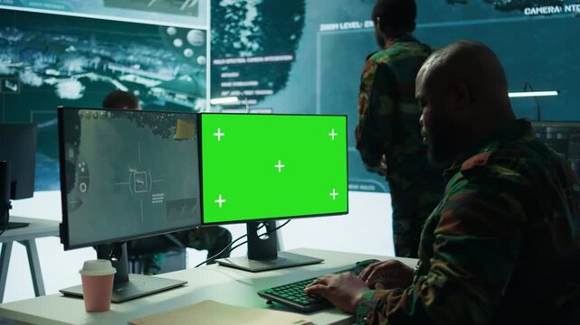 Army officer gathers intelligence from radar next to isolated copy space, working on satellite data monitoring from control room. Employs high tech gear and big screen in command post. Camera B.