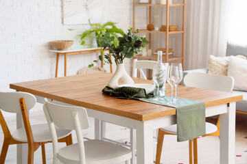Vase with eucalyptus branches and glasses on dining table in room