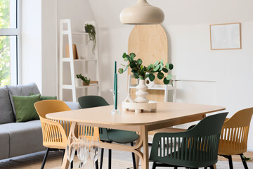 Vase with eucalyptus branches and candles on dining table in room