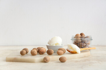 Board with shea butter and nuts on table against light background