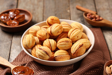 Bowl with tasty walnut shaped cookies and boiled condensed milk on wooden table, closeup