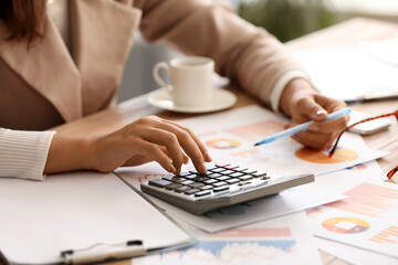 Young businesswoman working with documents and calculator at workplace in office, closeup