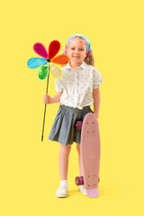 Cute little girl with toy windmill and skateboard on yellow background