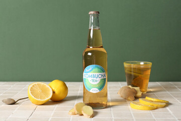 Bottle and glass of tasty kombucha tea with lemon and ginger on beige tile table