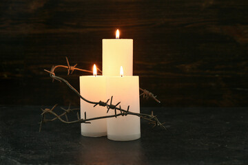 Burning candles with barbed wire on dark background. Day of Remembrance