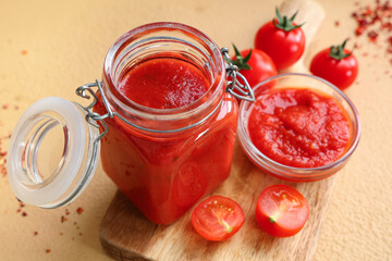 Jar and glass bowl of tomato sauce on brown background