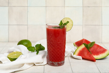 Glass of fresh watermelon juice with lime and mint on white tile background