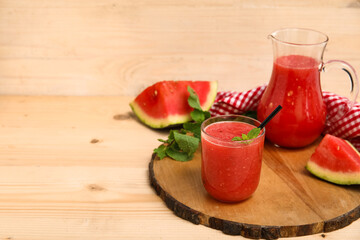 Glass and jug of fresh watermelon juice with mint on wooden background