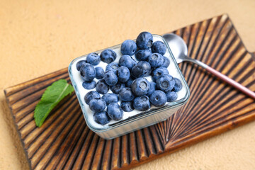 Glass bowl of tasty yogurt with fresh blueberries on brown background