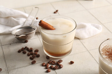 Glass of White Russian cocktail with cinnamon and coffee beans on white tile table