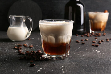 Glass of White Russian cocktail with coffee beans and jug of cream on black background