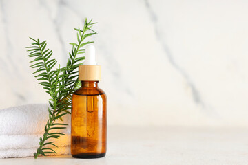 Bottle of essential oil, fir branch and towels on light background