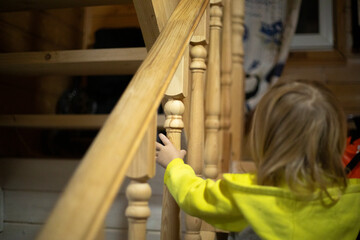 The child climbs the stairs. Stairs to the second floor in the house. The child holds on to the railing.