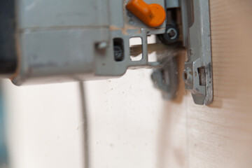 Electric jigsaw cutting wood plank in workshop