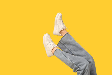 Legs of young woman in stylish white sneakers on yellow background