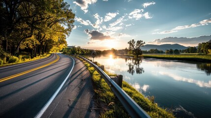 Obraz premium Scenic road alongside a tranquil river at sunset, framed by lush trees and vibrant clouds, creating a peaceful nature landscape.