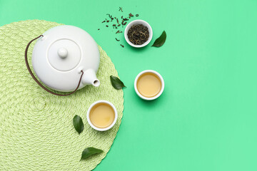 Bowls and teapot of hot tea with dried leaves on green background