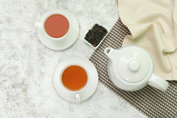 Cups and teapot of hot tea with dried leaves on white background