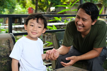 A happy young boy in a white shirt enjoys quality time with his smiling father in an outdoor setting. This image is ideal for content related to family bonding, father-son relationships, parenting,