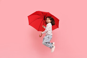 Cute little girl with red umbrella on pink background