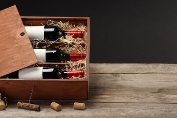 Box with wine bottles, corkscrew and corks on wooden table against black background. Space for text