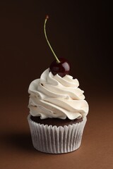 Delicious cupcake with cream and cherry on brown background