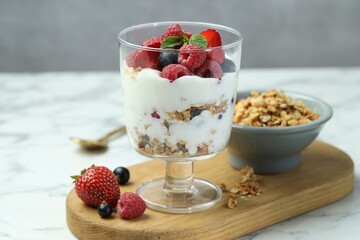 Tasty yogurt with fresh berries and granola in glass dessert bowl on white marble table, closeup