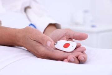 Senior woman with emergency call button on bed, closeup