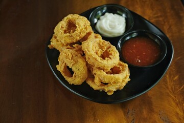 Crispy onion rings served with two dipping sauces on a black plate. Perfect for food blogs, restaurant menus, and snack advertisements showcasing delicious appetizers and comfort food.