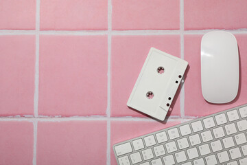 Computer keyboard with mouse and cassette on a pink background