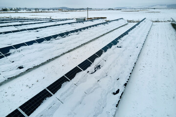 Aerial view of sustainable electrical power plant with solar photovoltaic panels covered with snow...