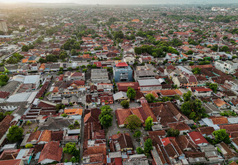 an aerial view of Yogyakarta city of a densely packed cityscape with a mix of traditional and modern buildings, lush greenery, and winding streets at sunset.