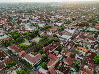 An aerial view of a dense urban area showcases a vibrant modern buildings, surrounded by greenery and bustling streets at sunset