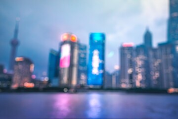 A blurred image of skyscrapers in a city, with a reflective body of water in the foreground and a cloudy sky as the background.