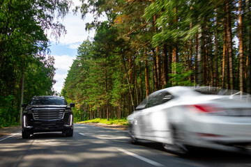 A  gray  new  SUV is driving along a highway in the forest, with blurred cars