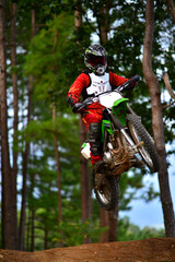 Motocross racing in the forest. One of the reacer in red racing suite jumping the bike with the mound and fly in the air