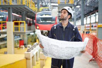 Engineer or worker reading and checking blueprint paper at construction train station
