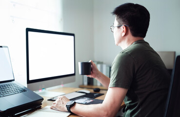 Man working form home, using desktop computer and laptop, drinking coffee stay at home.