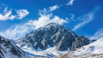 Obraz premium Majestic mountain peak with snow-covered slopes, standing tall under a bright blue sky with a few scattered clouds