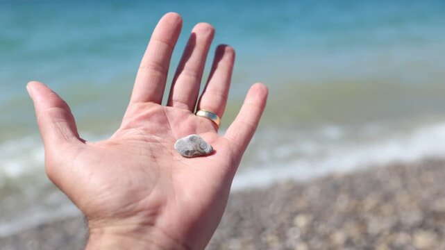 Hand holding a Petoskey stone above blue waves on a beach