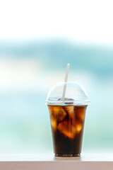 Iced Americano in a take-out plastic cup. Window with a panoramic view