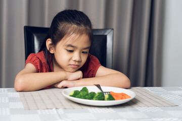 Little cute kid girl refusing to eat healthy vegetables. Children do not like to eat vegetables.