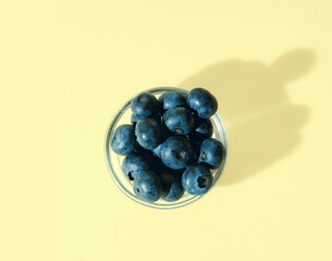 Fresh Blueberries in a glass bowl on a light yellow background, flat lay,  minimal summer fruits concept