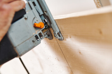 Carpenter cutting wood plank using jigsaw in workshop
